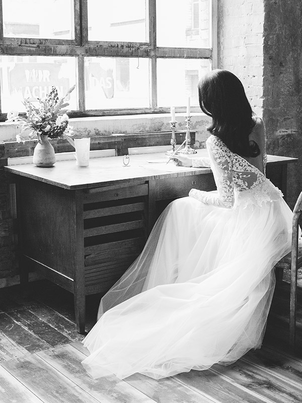 Braut von hinten sitzt im Hochzeitskleid am Tisch und schreibt Hochzeitsfotografin Berlin