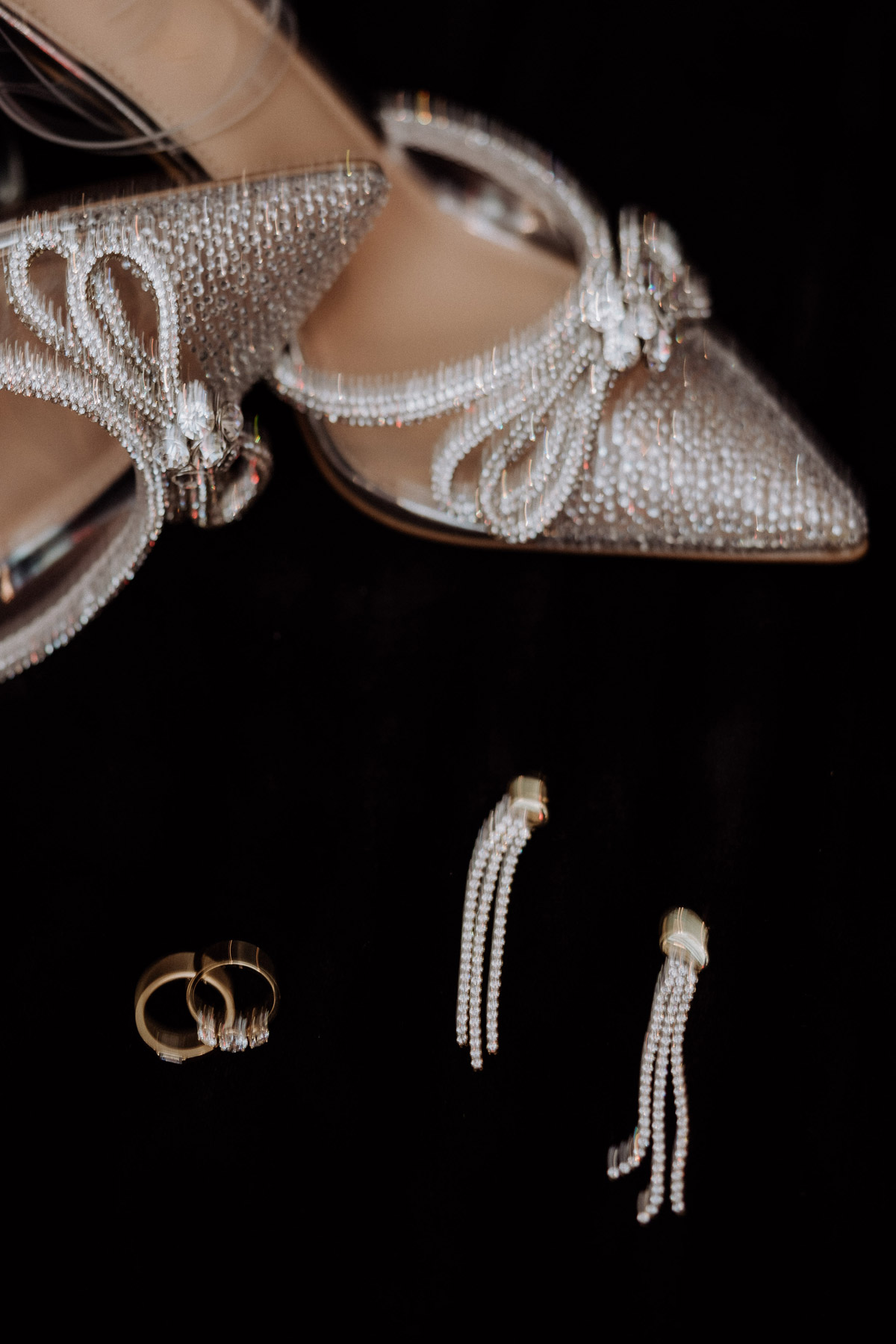 Glitzernde Designer-Brautschuhe mit Schleife und Eheringe auf dunklem Samt, High End Hochzeitsdetails. Foto: Melanie Meißner