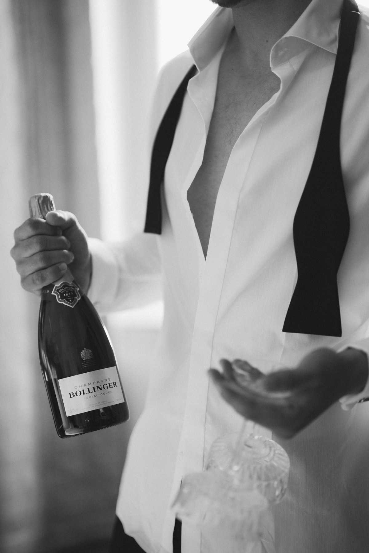 Bräutigam hält beim Getting Ready zur Hochzeit Champagnerflasche und Gläser in der Hand