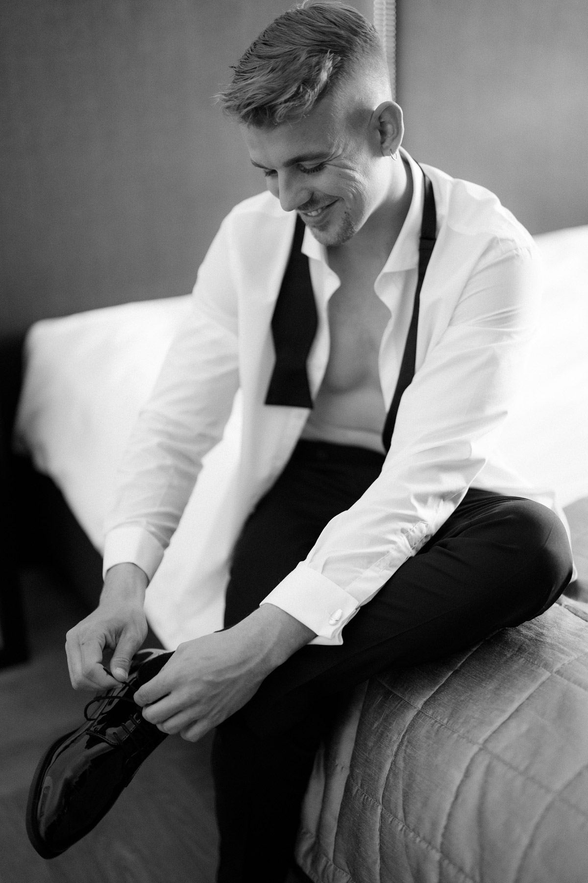 mit offenem Hemd und offener Fliege bindet der Bräutigam seine Schuhe