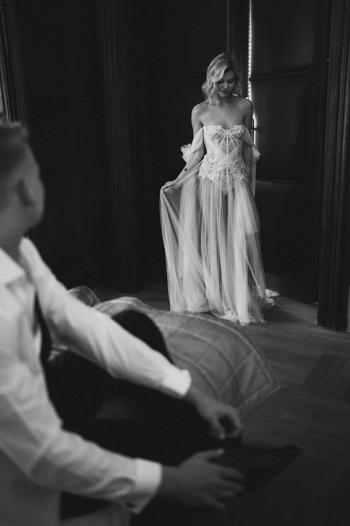 Braut überrascht Bräutigam mit ihrem ersten transparenten Hochzeitskleid im Türrahmen stehend