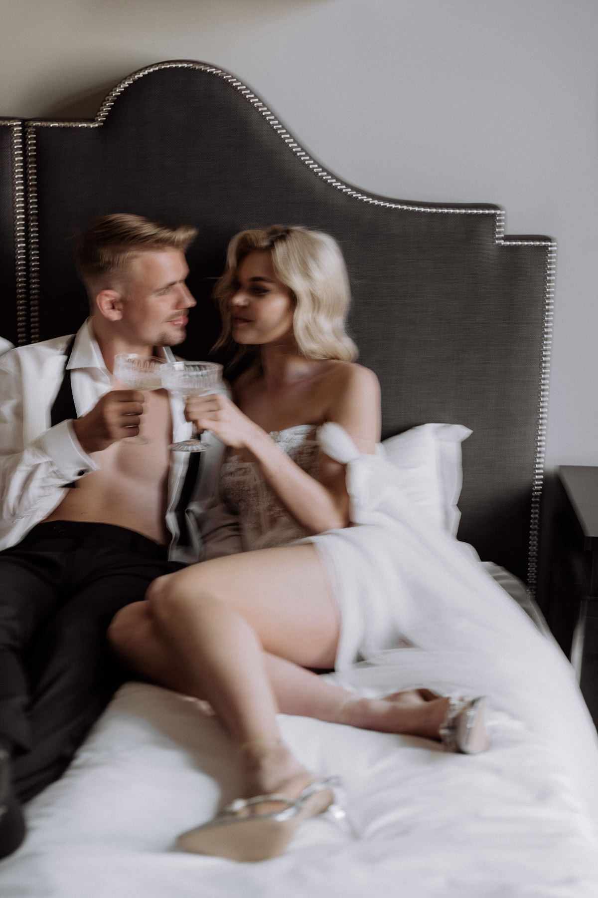 Hochzeitspaar sitzt im Bett und stößt mit Champagner an
