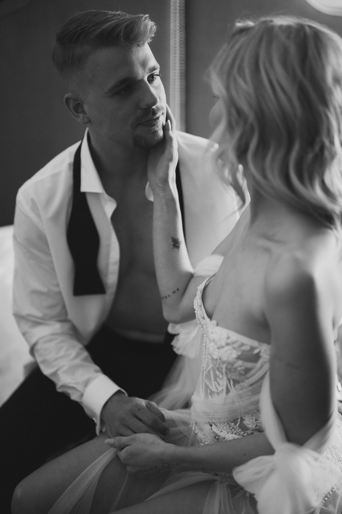 sinnliches Bräutigamportrait mit unscharfer Braut die über seine Wange streichelt