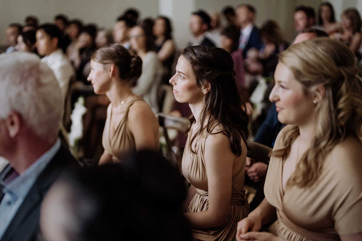 Brautjungfern sitzen bei Hochzeitsgästen und verfolgen die Trauzeremonie