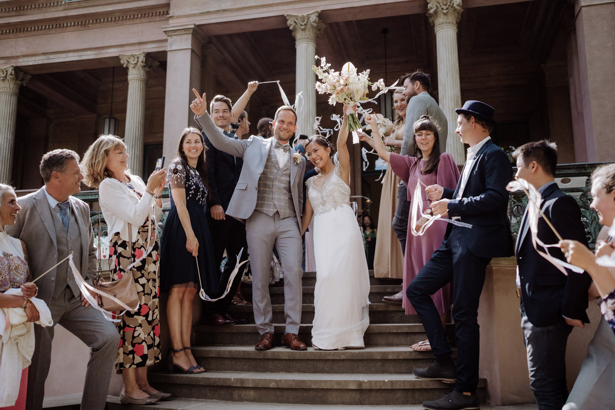 Schloss Biesdorf Hochzeit: Brautpaar steht mit Gästen jubelnd auf Treppe