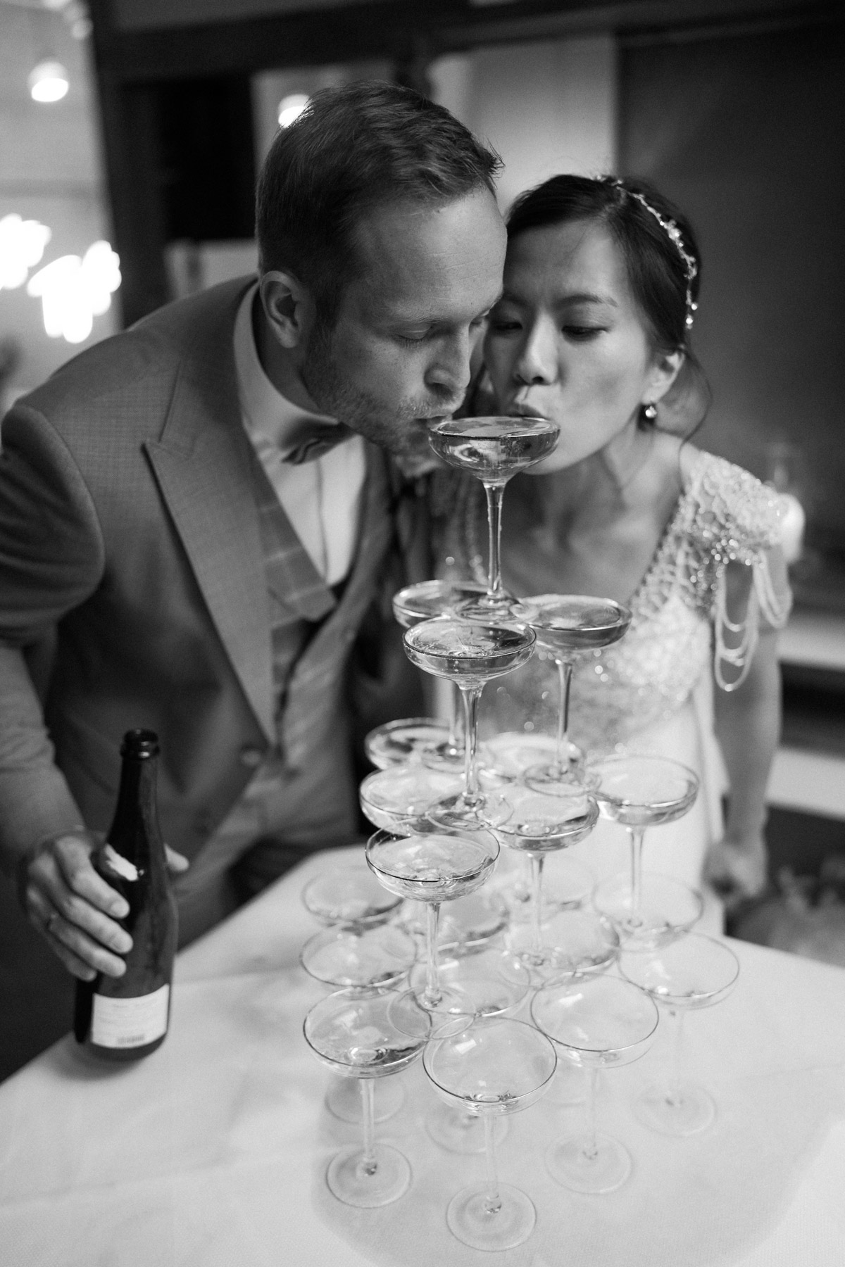Restaurant Berlin Hochzeit: Cooles Brautpaar trinkt von Champagnerpyramide im heimlichTreu