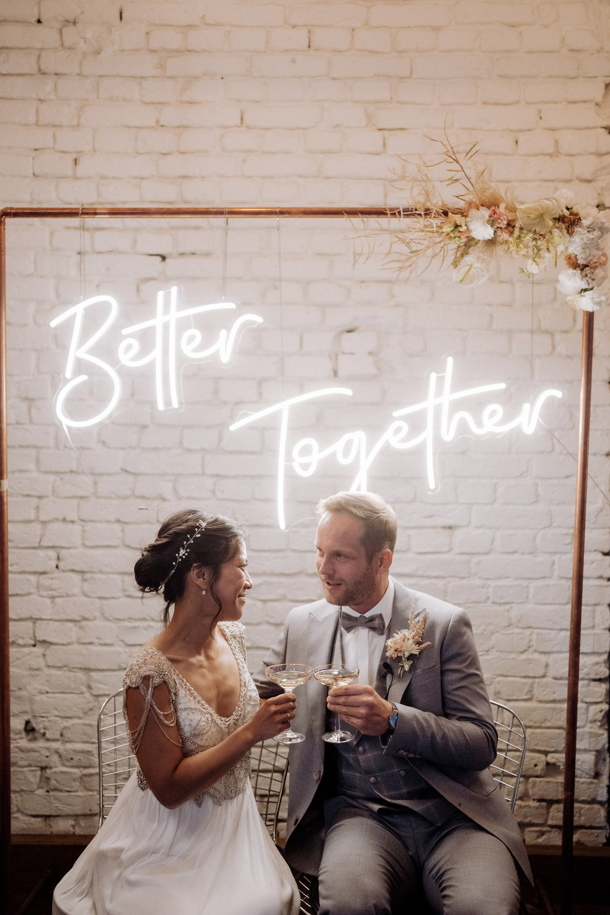 Modernes Brautpaar Berlin sitzt vor Better Together Schild und trinkt Champagner