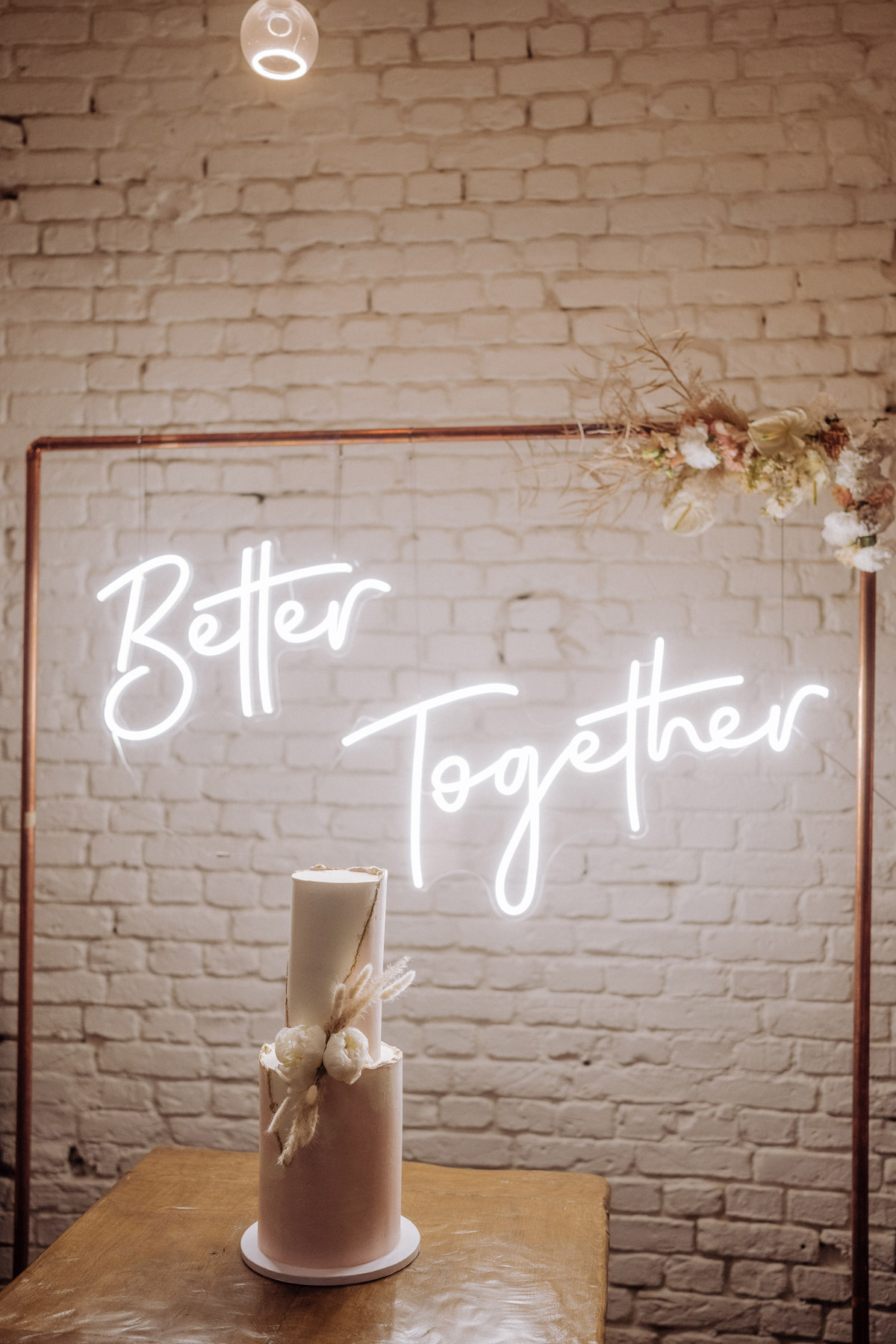 zweistöckige Hochzeitstorte in Rosa und Weiß vor Better Together Leuchtschrift