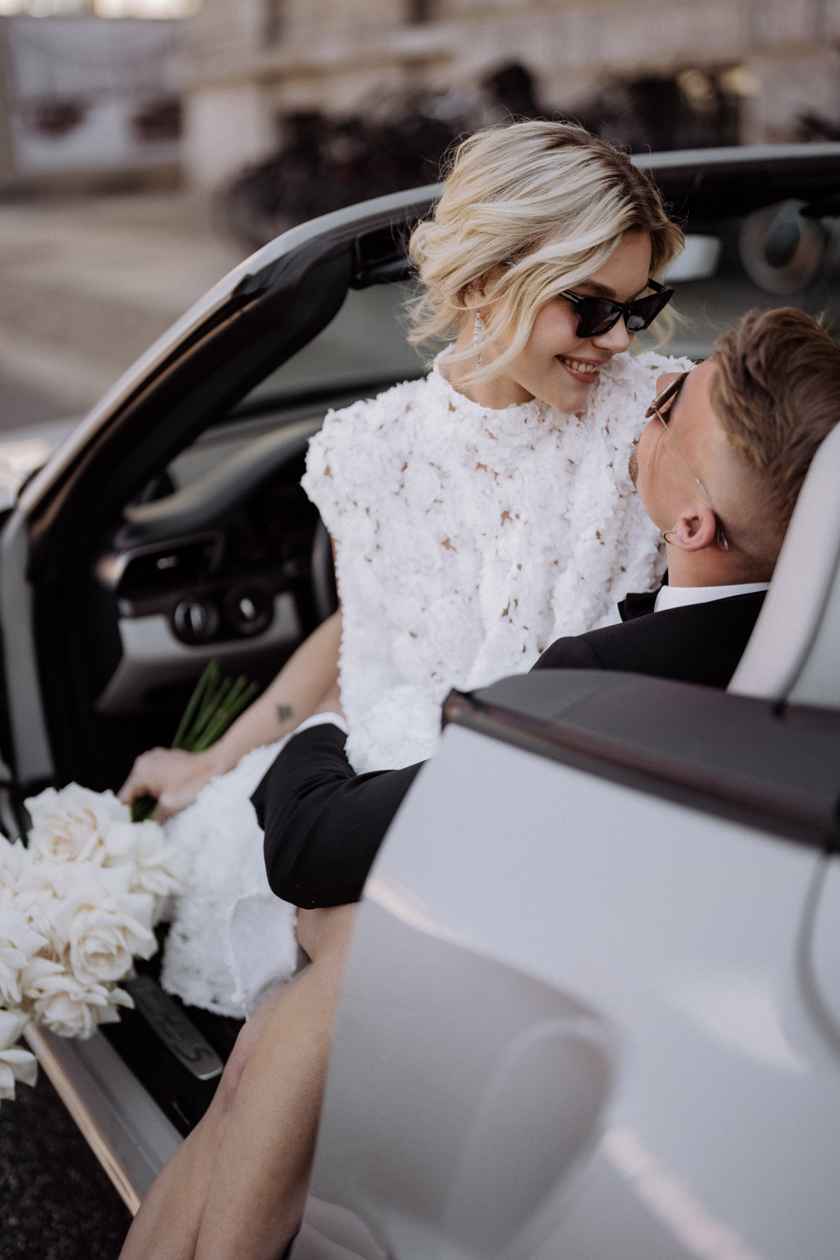 Braut sitzt auf Schoß vom Bräutigam und lacht