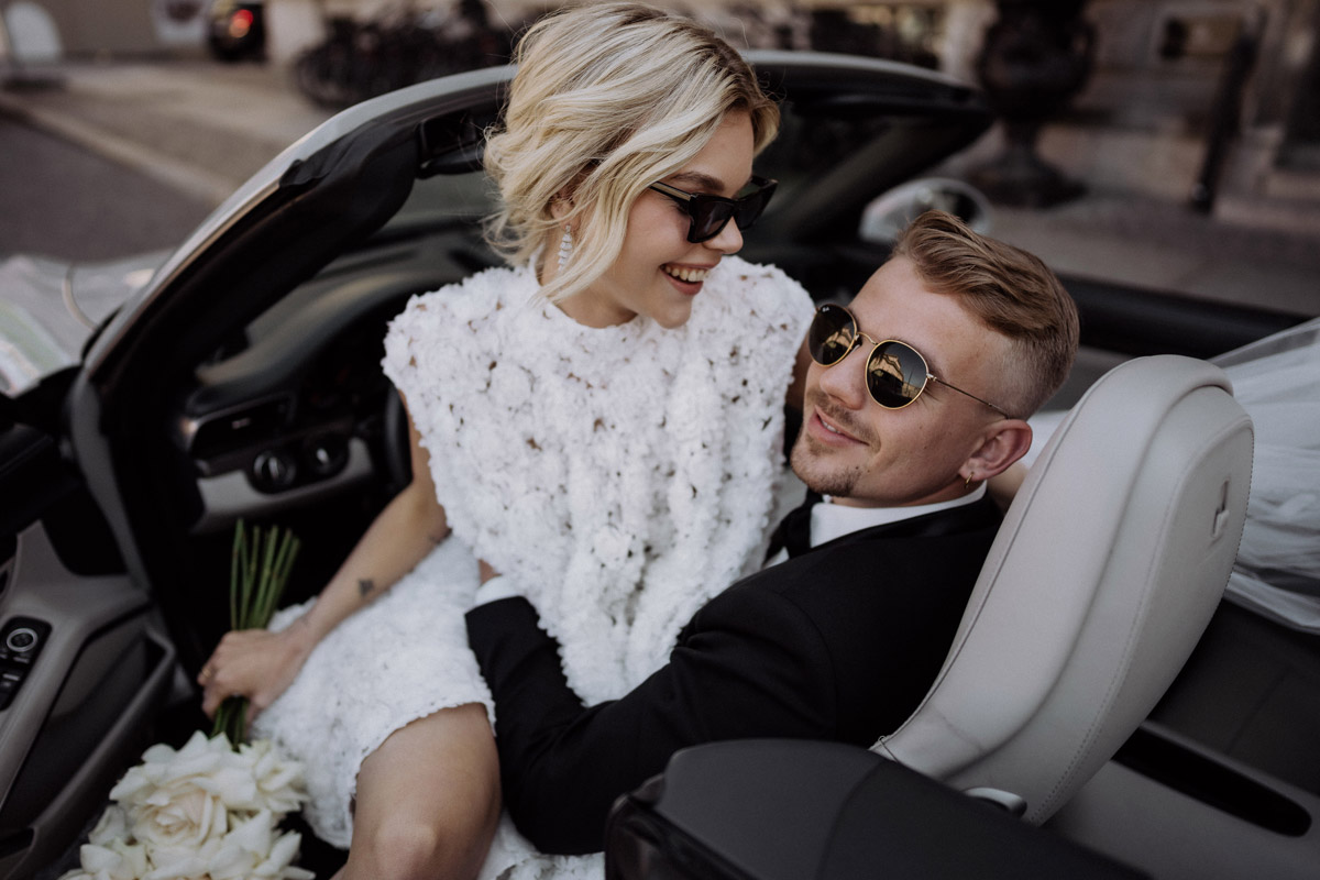 Editorial Hochzeitsfotografie von Paar mit Sonnenbrillen im Auto auf dem Weg zum Berlin Mitte Standesamt