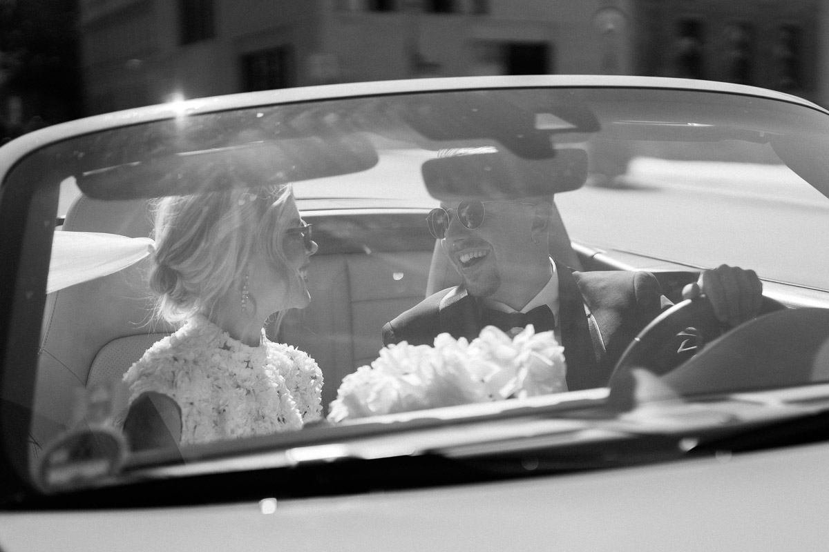 Paar lacht sich während der Fahrt an, Perspektive durch die Frontschreibe des Cabrio Hochzeitsauto