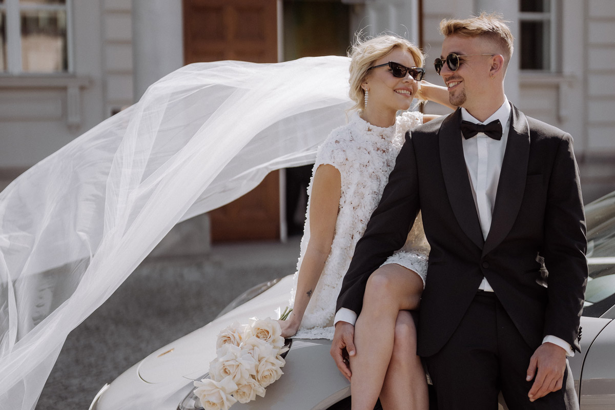 Editorial Hochzeitsfotos Standesamt Berlin Mitte: Cooles Brautpaar mit Sonnenbrillen und wehendem Schleier auf einem Auto. Vorab-Infos zu Outfits helfen bei der Planung solcher Lieblingsmotive.