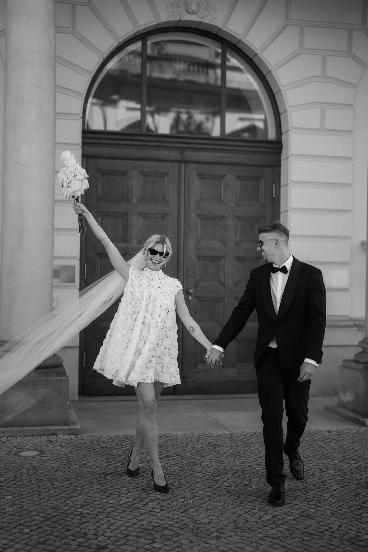 Hochzeitsreportage Standesamt Berlin Mitte Auszug: Braut streckt feiernd den Brautstrauß in die Luft