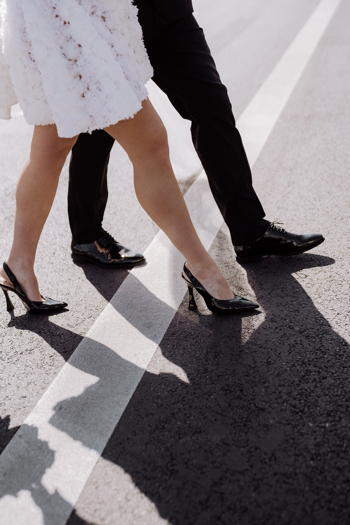 schwarze Brautschuhe zum kurzen Standesamtkleid überqueren mit schwarzen Bräutigamschuhen die Straße