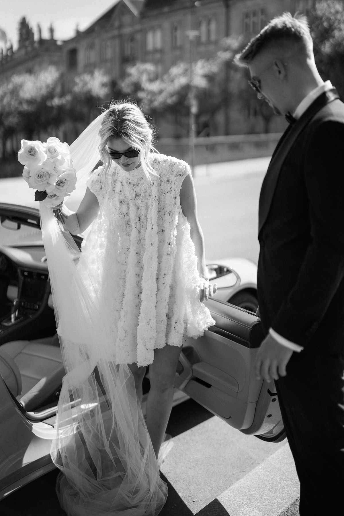 Bräutigam hilft Braut ins Auto zu steigen