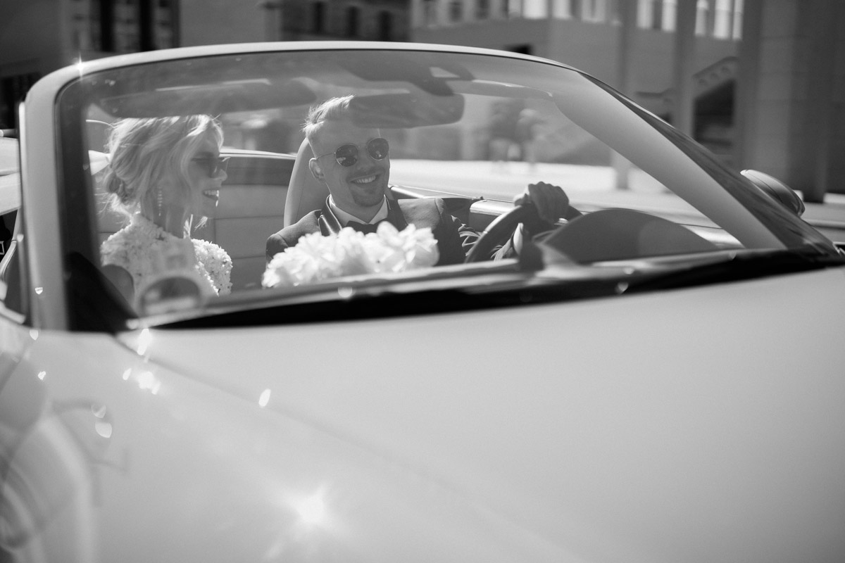 Just Married Vibes Berlin Mitte: Lachendes Brautpaar im offenen Cabrio nach dem Standesamt