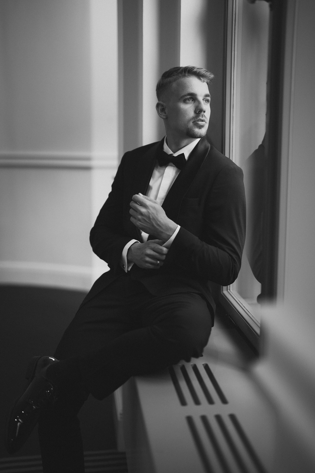 Bräutigam schaut beim Korrigieren seiner Ärmel aus dem Fenster