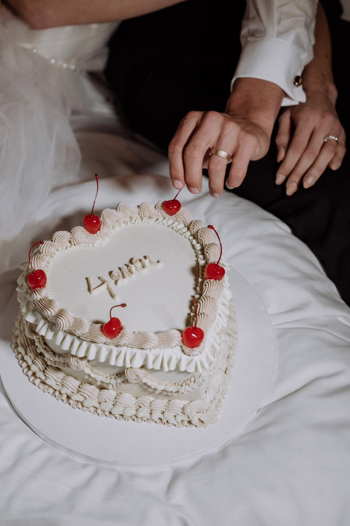 Statement Wedding Cake in Herzform: Hand des Bräutigams mit Ehering greift Kirsche von Torte