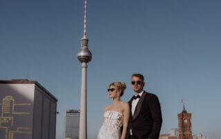 Bester Hochzeitsfotograf Berlin für moderne Paare: Brautpaar steht mit Sonnenbrillen vor dem Fernsehturm auf Rooftop des Humboldt-Forums