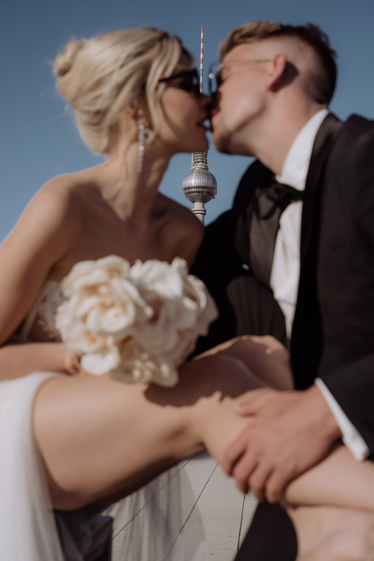 kreative Hochzeitsfoto-Idee: Hochzeitspaar küsst sich unscharf im Vordergrund und zwischen ihnen ist im Hintergrund der Berliner Fernsehturm scharf zu sehen