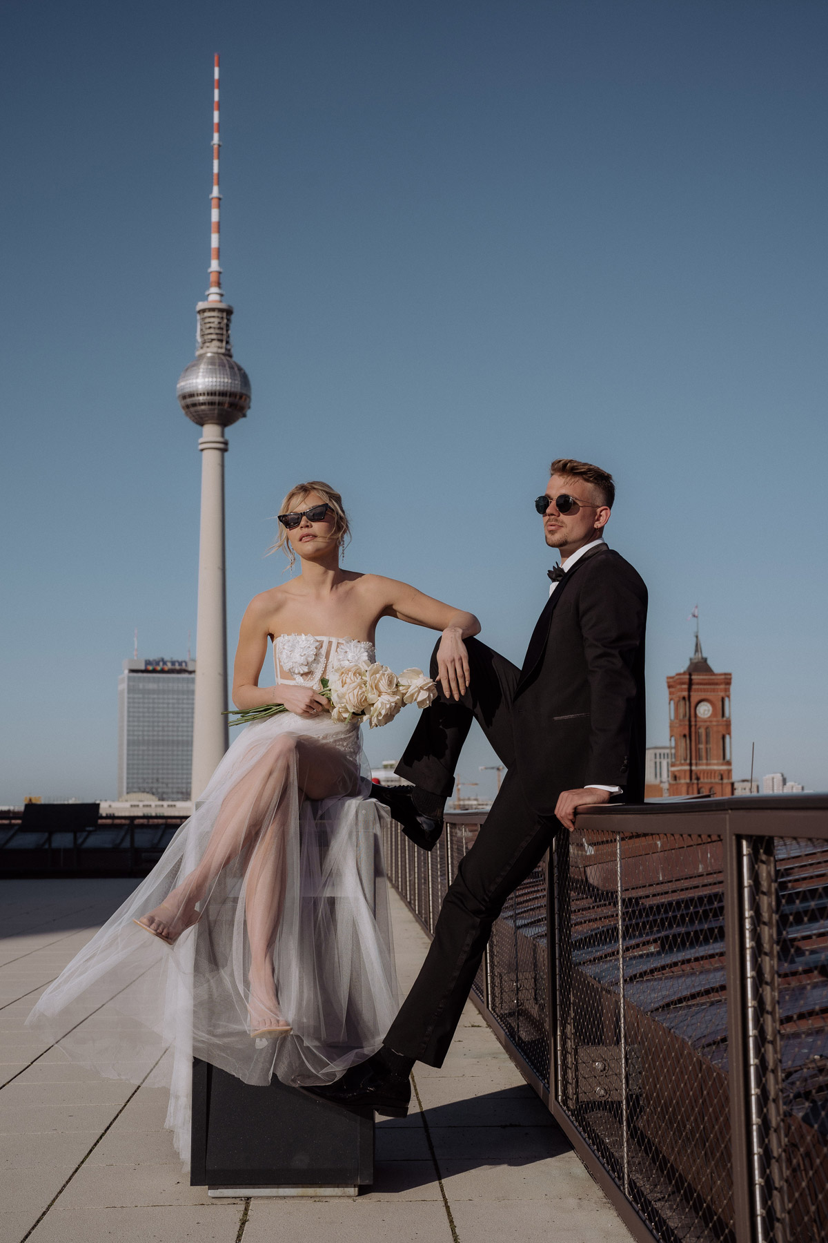 Modernes Brautpaar Fotoshooting in Berlin mit Skyline und Fernsehturm auf dem Geländer der Baret Dachterrasse von erfahrener Hochzeitsfotografin Berlin Melanie Meißner