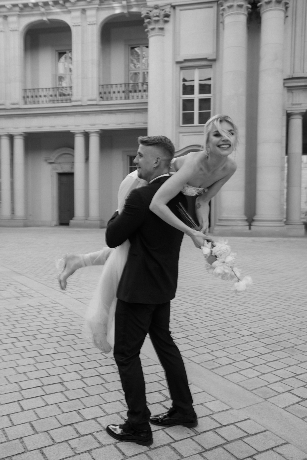 Hochzeitsfotografin Berlin fängt echte Emotionen und Spaß ein: Bräutigam trägt Braut im Innenhof des Berliner Schlosses