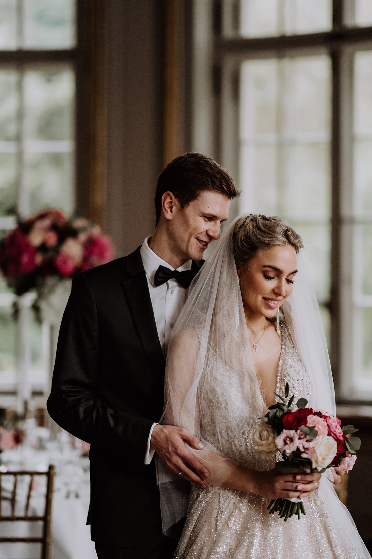 Tipp bei Regen auf der Hochzeit - macht das Hochzeitsfotoshooting im Festsaal: elegantes Paar schaut bewegt nach unten auf den Brautstrauß