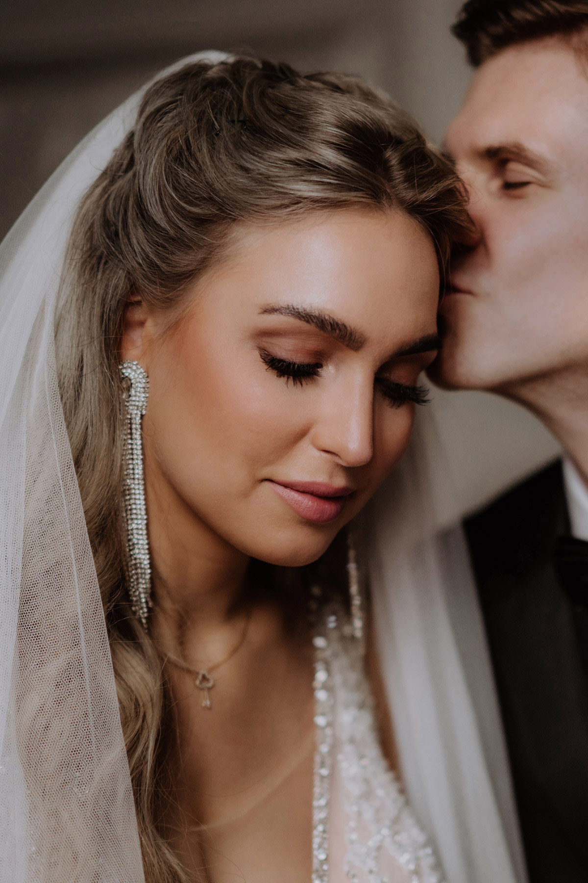 Braut Portrait mit küssendem Bräutigam im Hintergrund