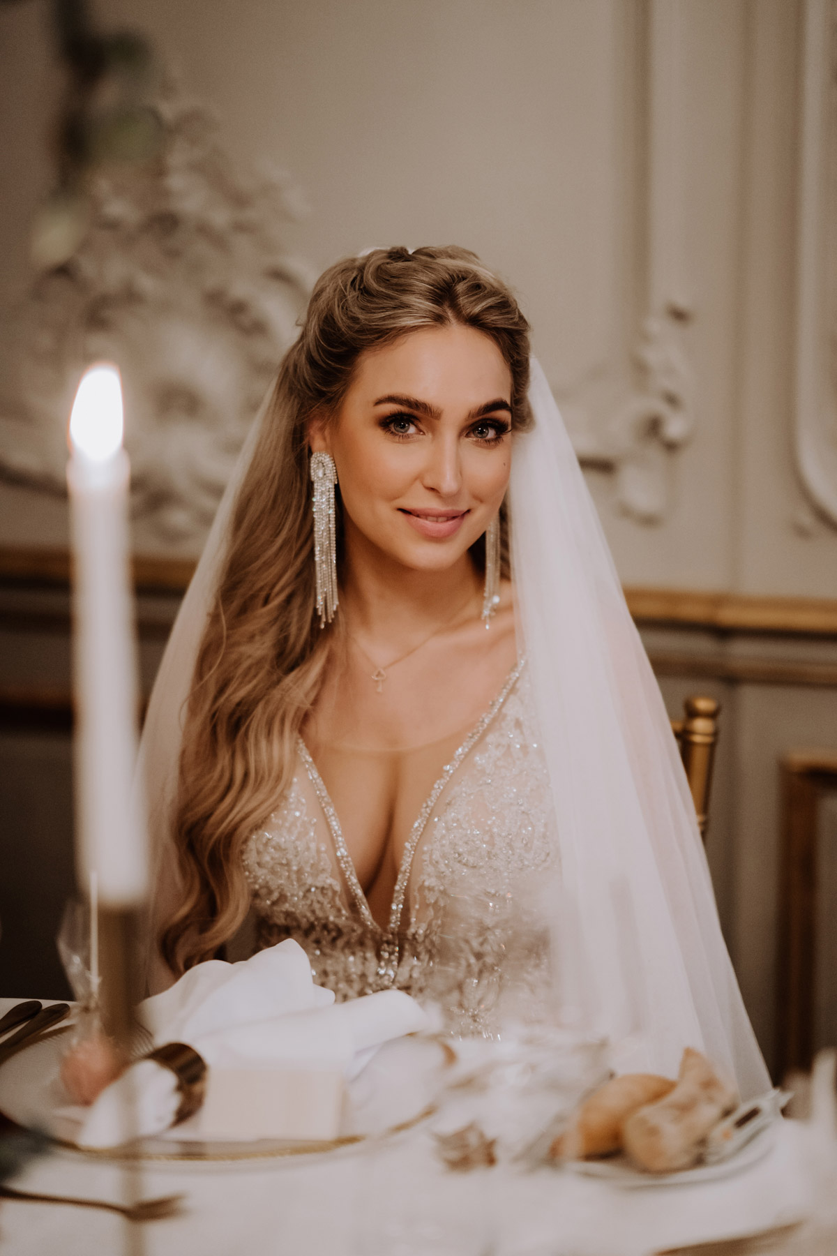 Braut sitzt am Hochzeitstisch und lächelt direkt in die Kameras des Foto- und Videoteams