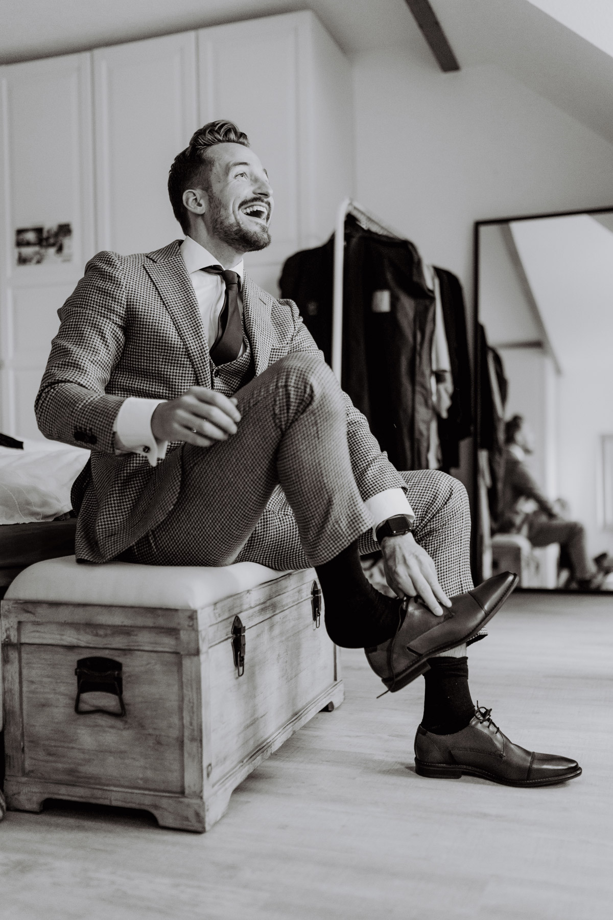 Bräutigam in kariertem Standesamt-Anzug zieht Schuhe an und lacht