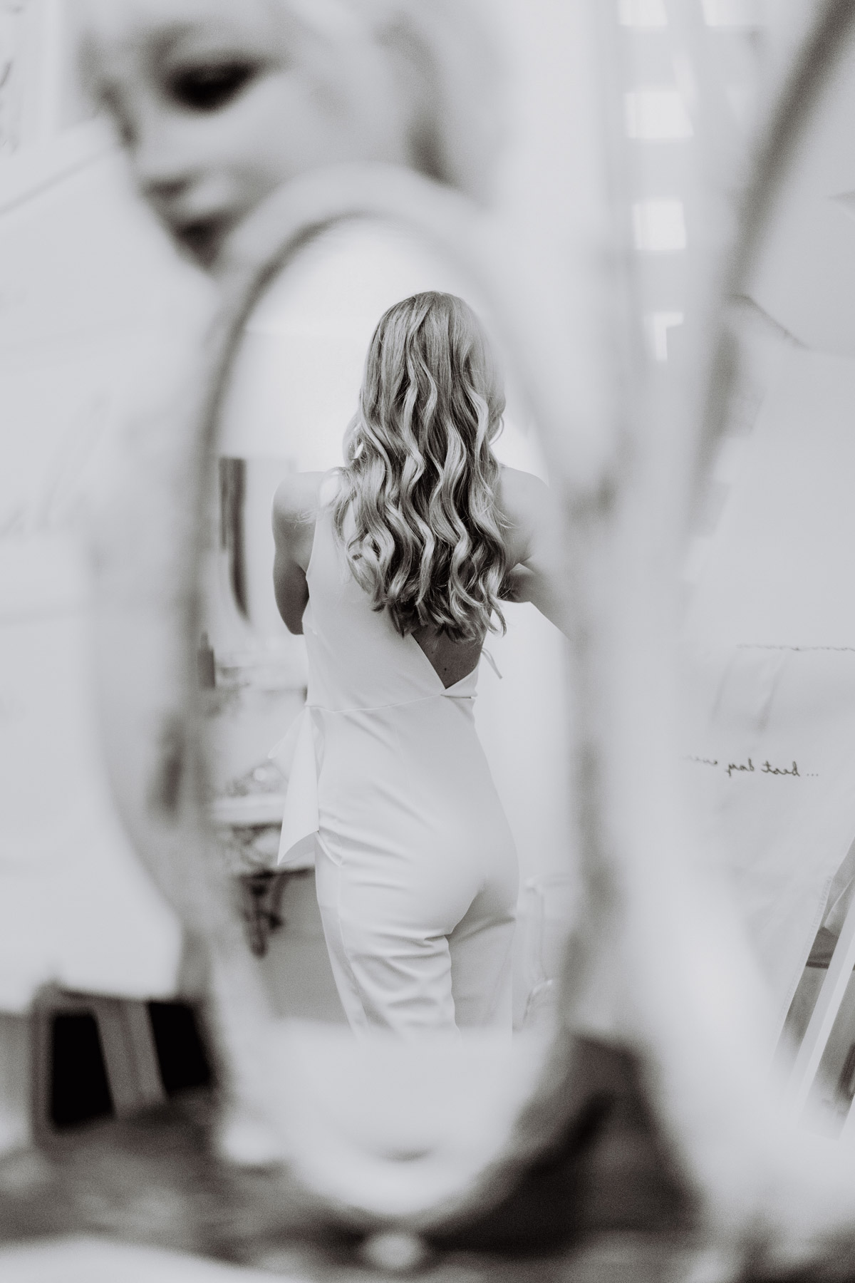 Weißer Jumpsuit für das Standesamt und kreatives Hochzeitsfoto: Braut von hinten im Spiegel beim Ankleiden fotografiert