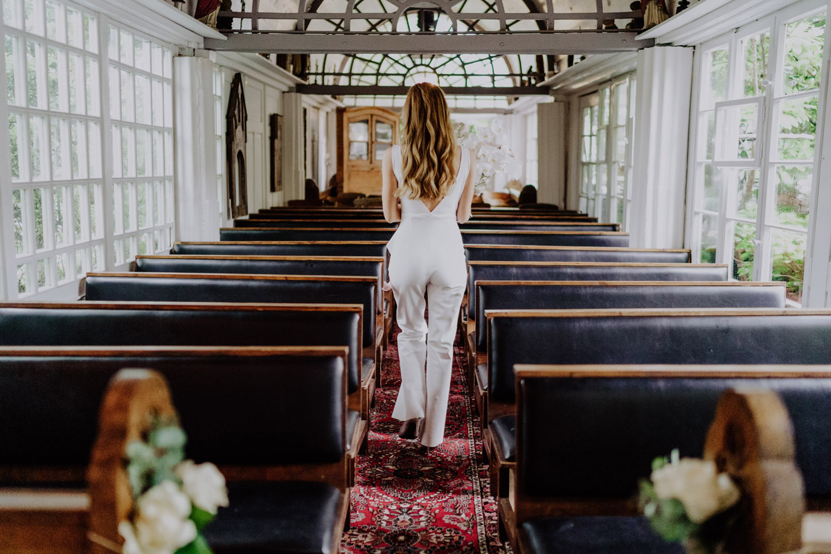 Braut von hinten im Jumpsuit geht auf Bräutigam für First Look zu