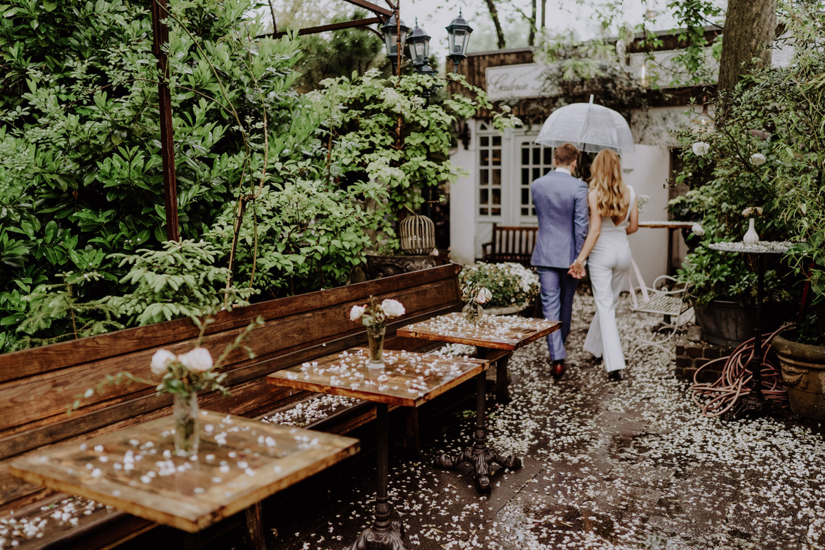 Brautpaar von hinten mit Regenschirm spaziert im Regen durch Berlin