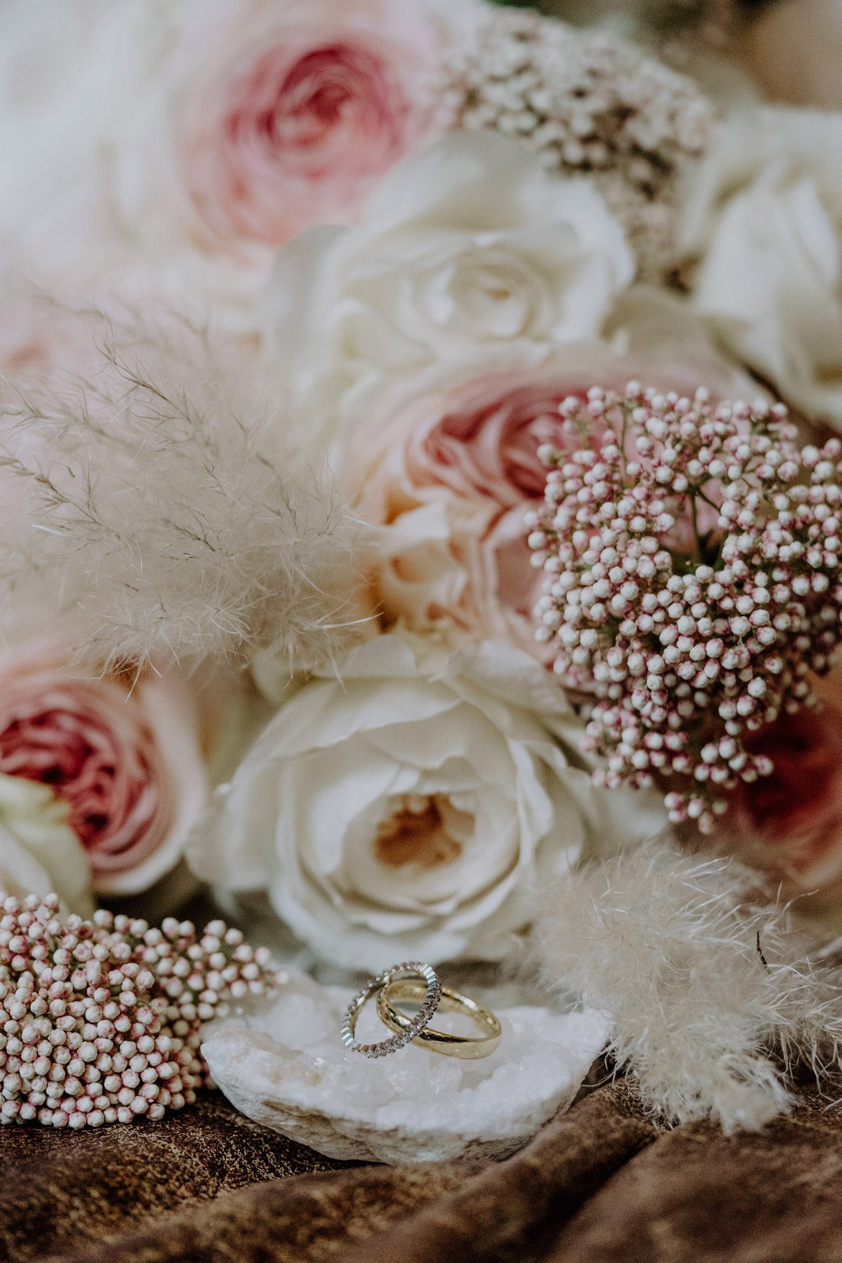 Eheringe in gold kunstvoll auf glitzernden Stein vor Brautstrauß positioniert