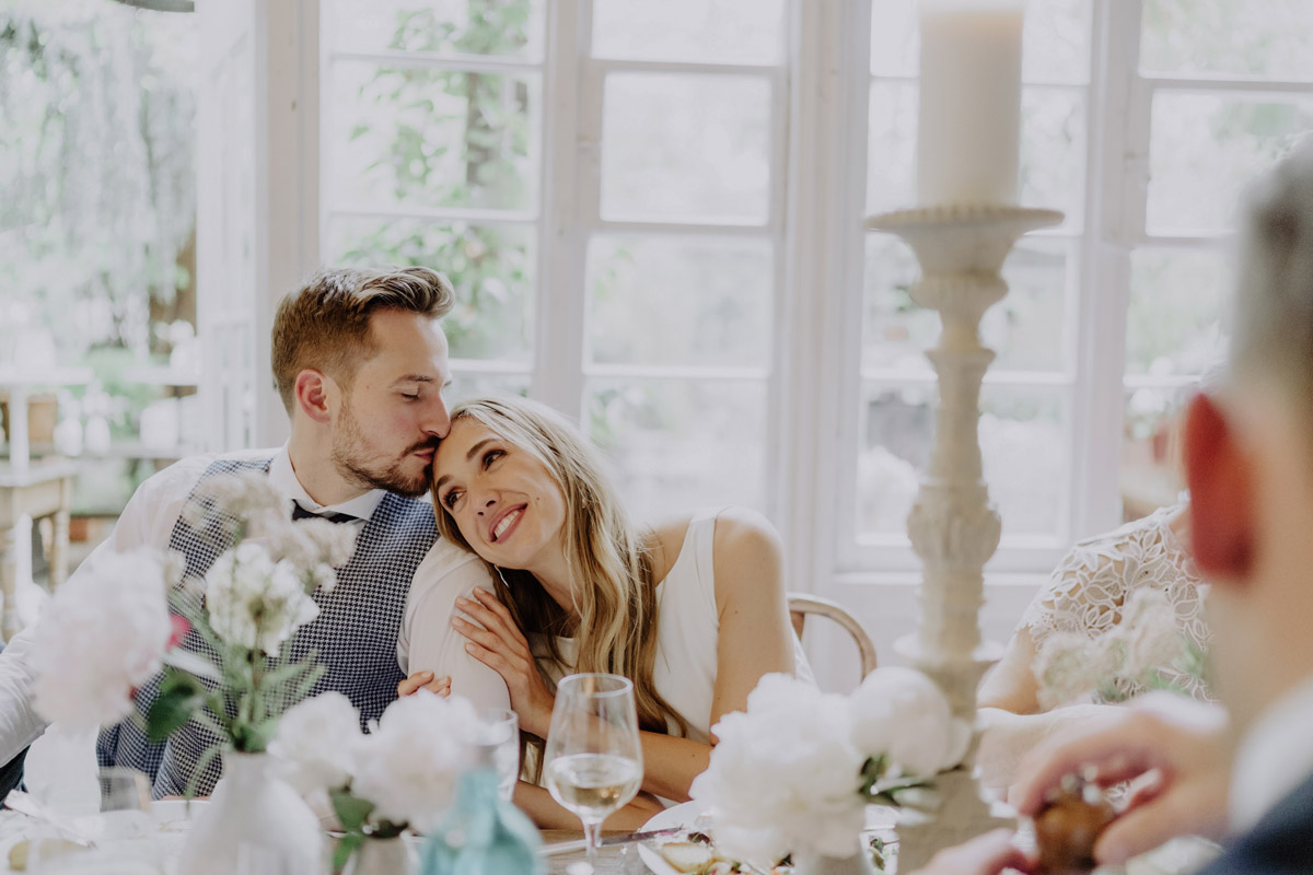 Hochzeit Berlin: Brautpaar am Tisch schmust verliebt während des Essens