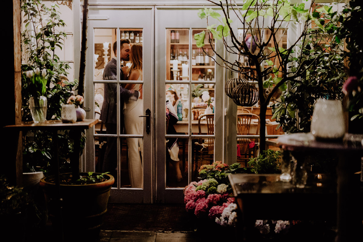 Kreativer Abschluss: Paar küsst sich in Location hinter Fenster, Standesamt Fotografin Berlin steht draußen im Regen