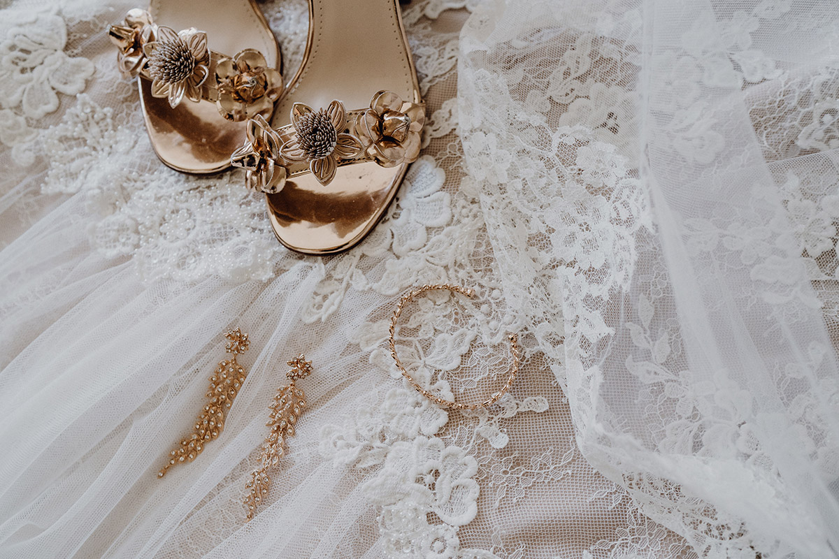 Flatlay: Brautschmuck und Schuhe in Rosegold auf Spitzenschleier arrangiert