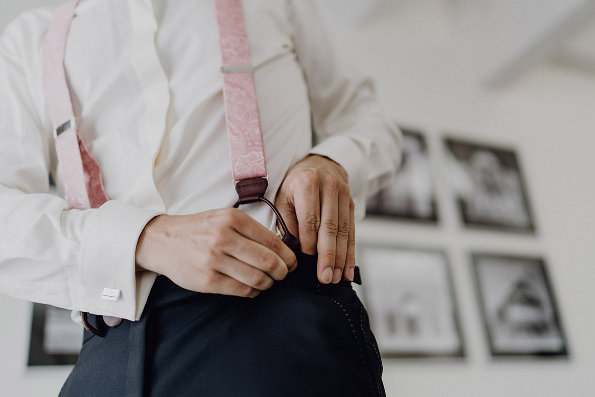 Bräutigam schließt Hosenträger beim Ankleiden