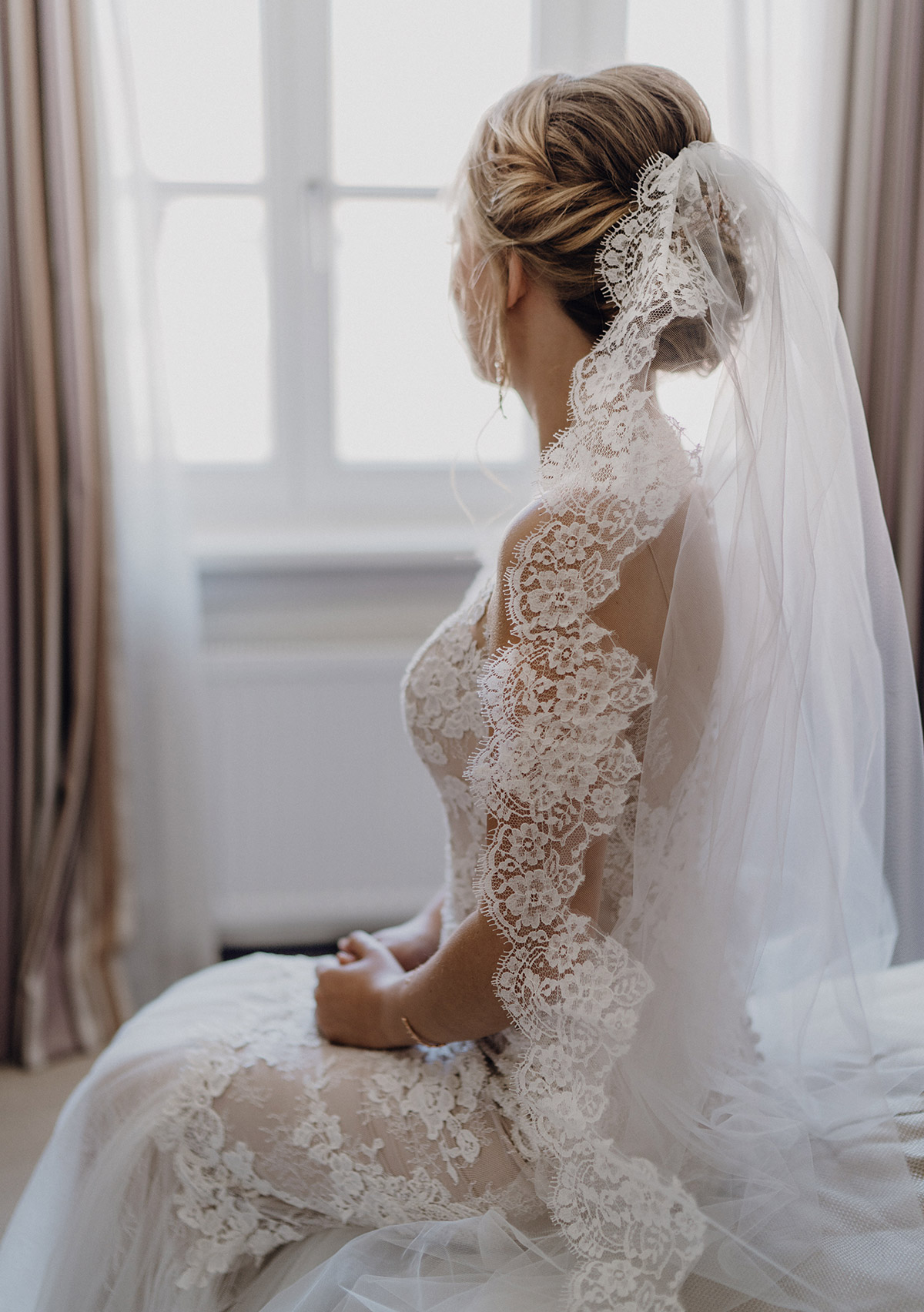 Braut mit Spitzenschleier von hinten sitzt auf Bett im Hotel Brandenburger Tor