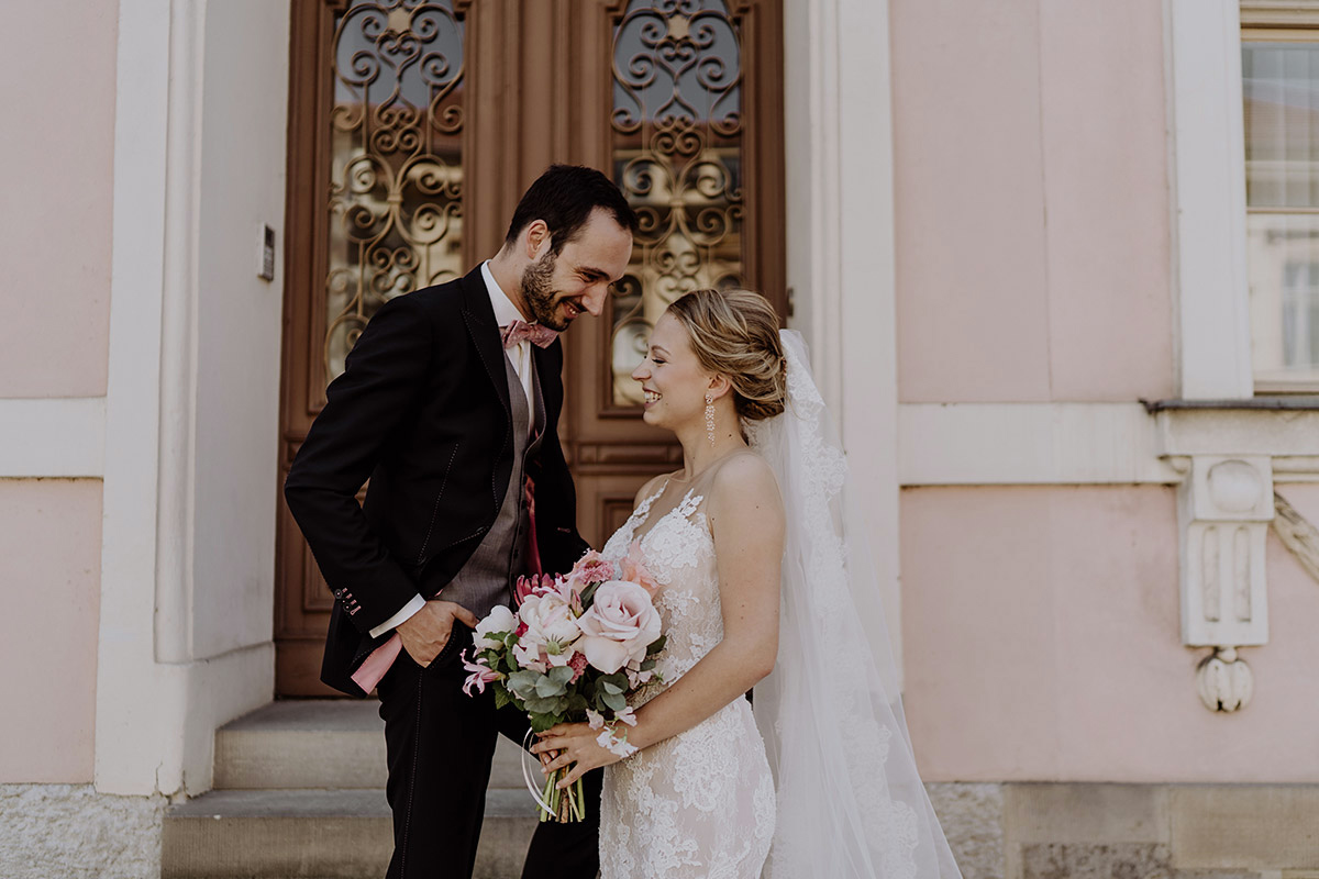 Hochzeitspaar lacht sich in Potsdam vor rosa Hausfassade an