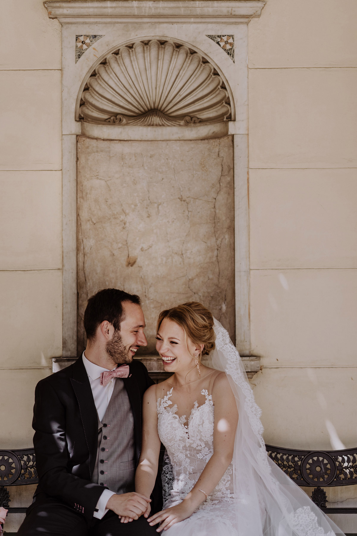 Zeitlose Hochzeitsfotografie: Paar sitzt auf Bank am Schloss Glienicke in Potsdam und lacht