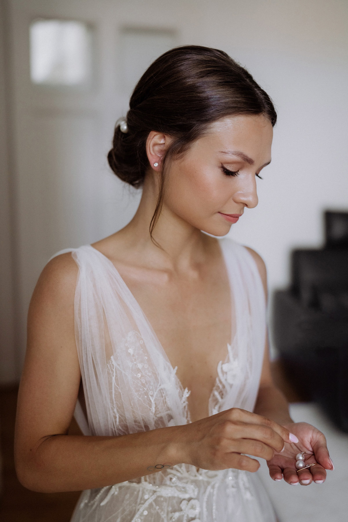 Braut mit natürlichem Make-up in einem Liz Martinez Hochzeitskleid betrachtet ihre Ohrringe vom Juwelier Lorenz Berlin – Fine Art Hochzeit Berlin