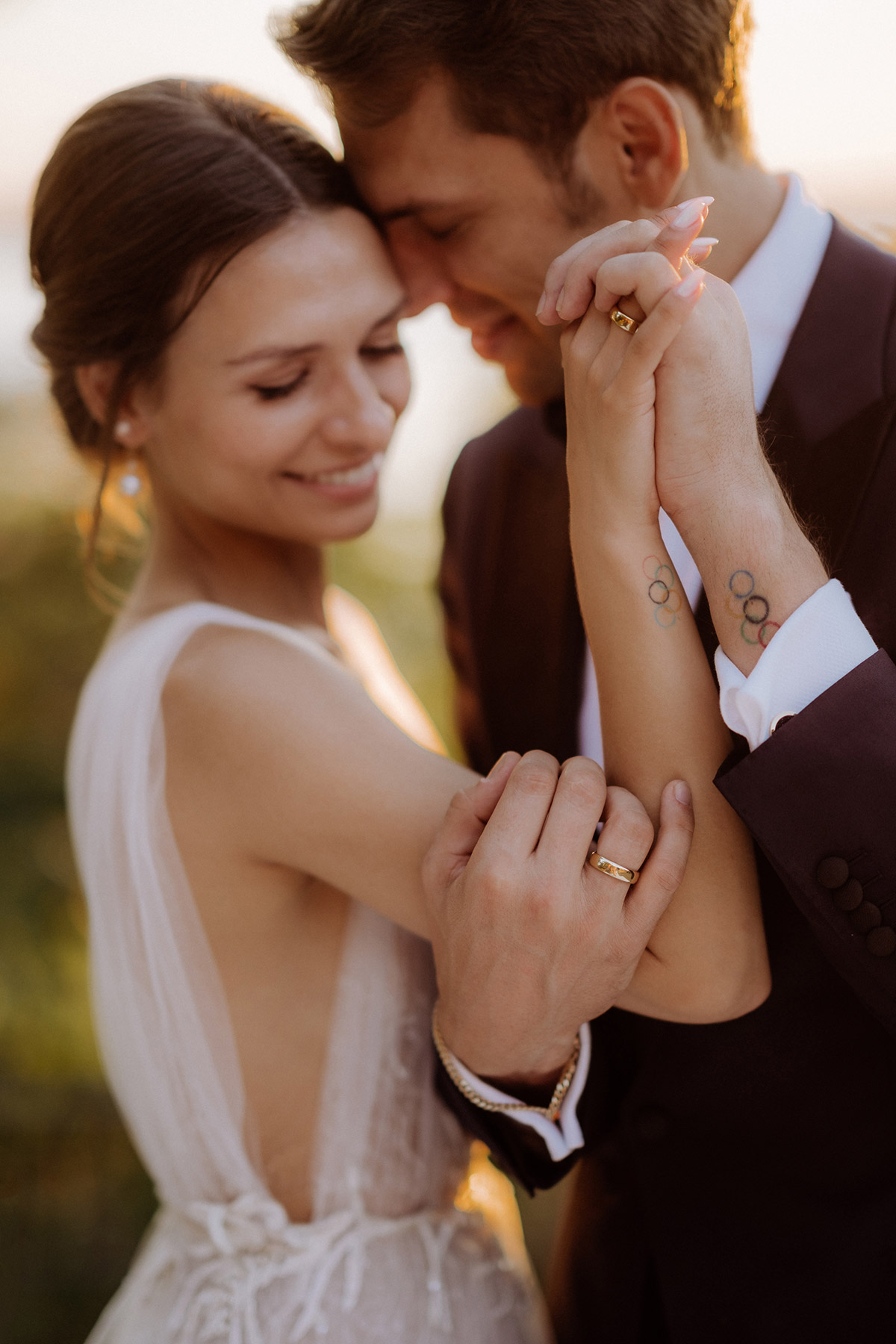 Goldene Eheringe an den Händen mit unscharfem Hochzeitspaar im Hintergrund