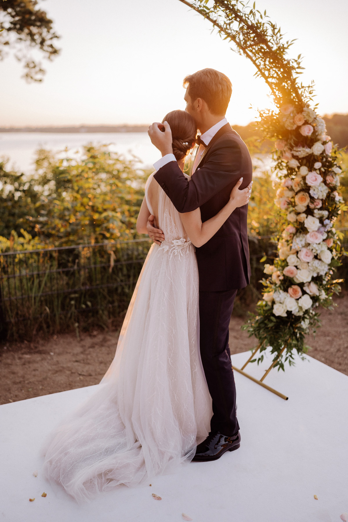 Rückenansicht des Brautpaares mit Blick auf den Wannsee: Eine natürliche Porträt-Idee bei der Hochzeit in den Wannseeterrassen Berlin.