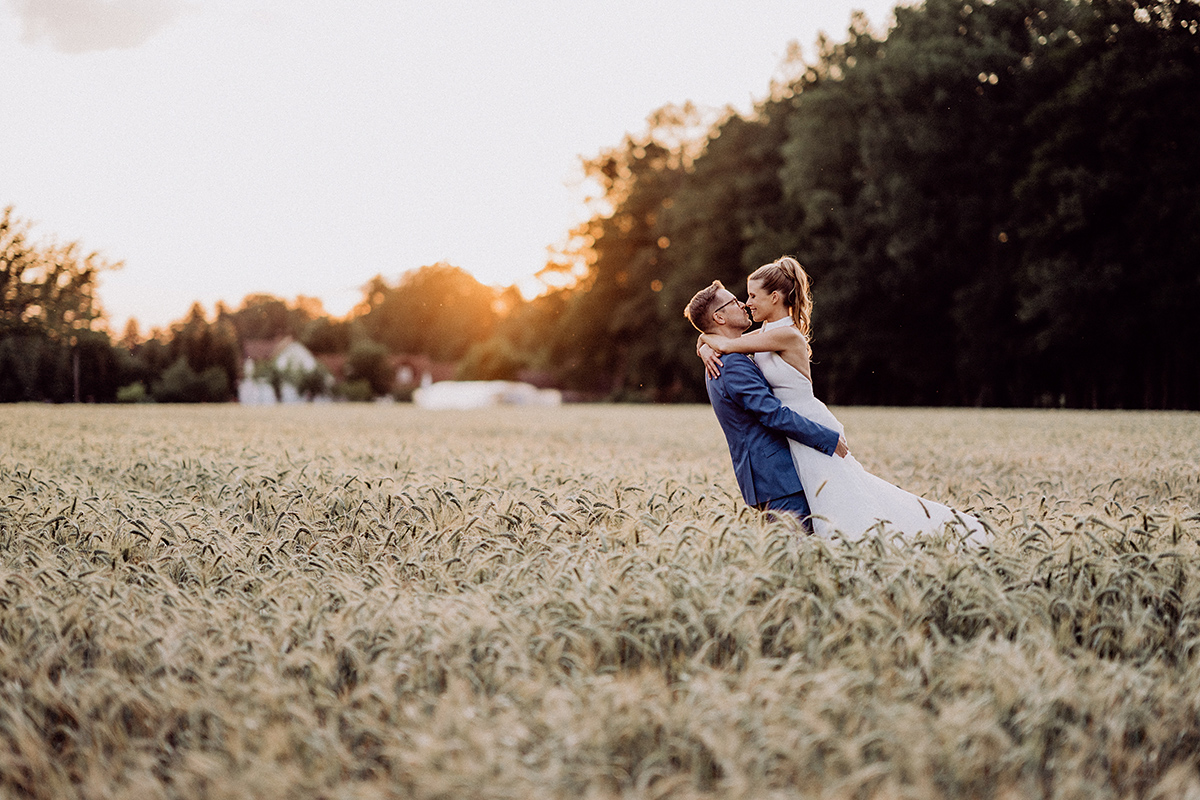 Brautpaar steht auf Feld vor dem Hotel Bleiche Resort & Spa im Spreewald – moderne Standesamt Hochzeitsfotografie.