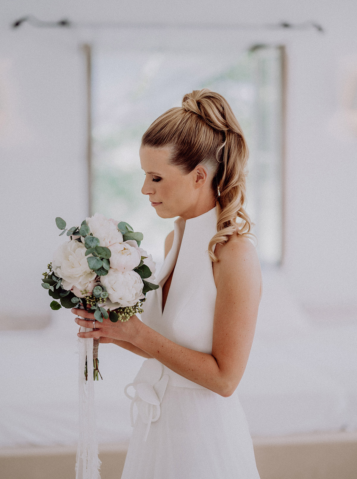 Braut mit hohem Pferdeschwanz und Brautstrauß mit Pfingstrosen und Eukalyptus