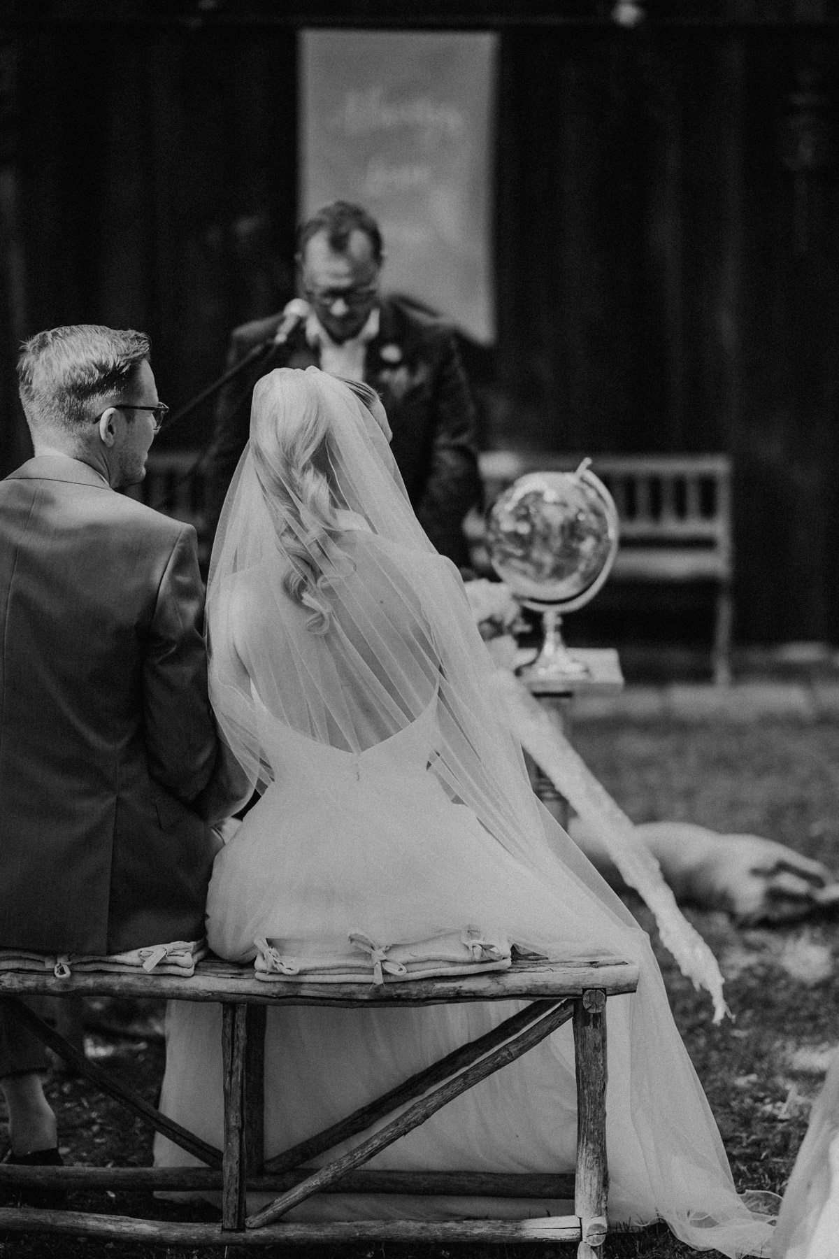 Brautpaar von hinten sitzt auf Bank unter freiem Himmel zur Standesamt-Trauung