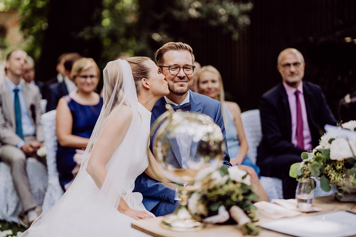 Braut küsst Bräutigam auf Wange bei Trauung