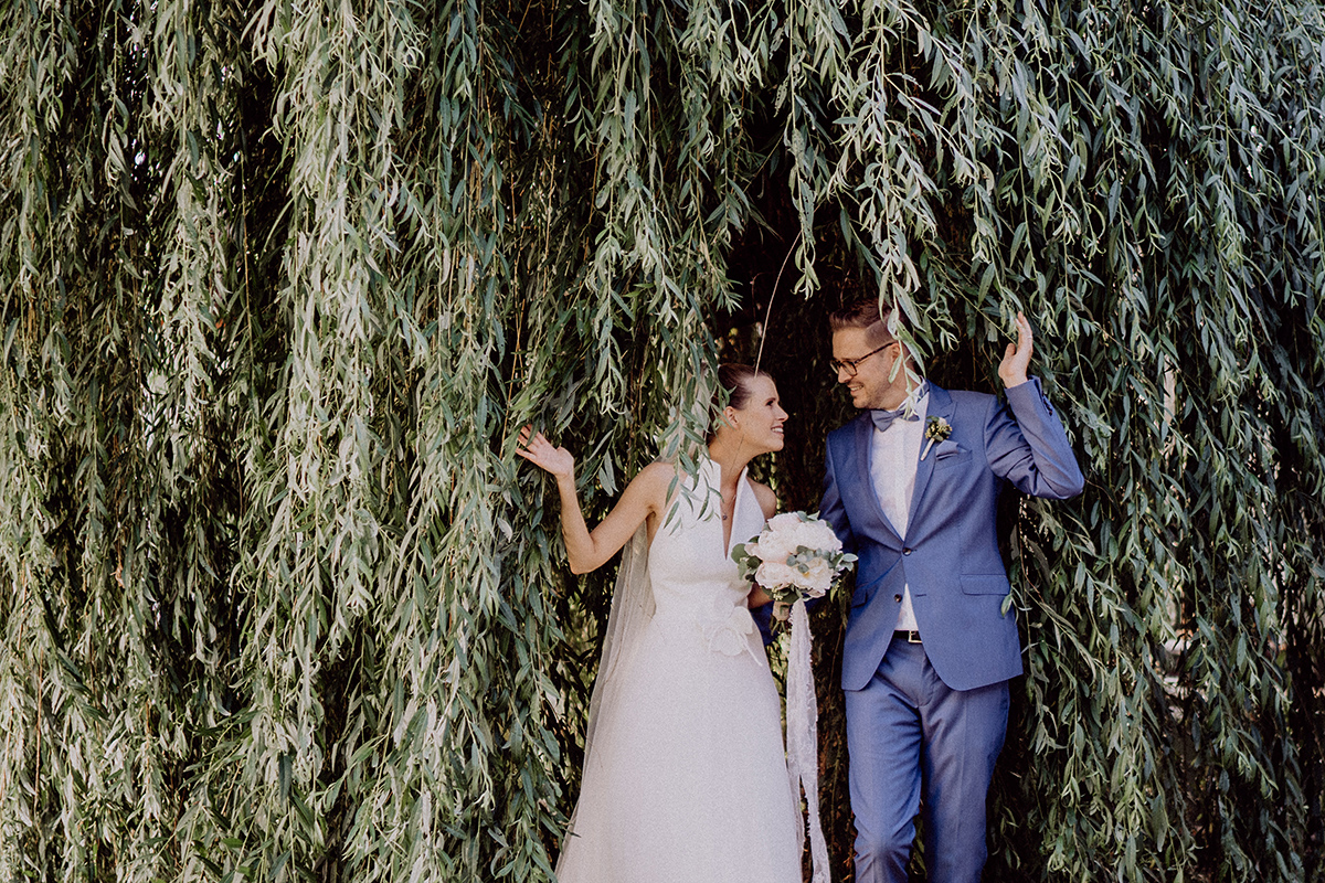 Brautpaar steht unter Trauerweide im Spreewald und lacht sich an