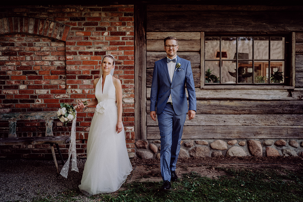 kreative Braut-Paar-Shooting Idee: Braut vor Backsteinwand und Bräutigam vor Holzwand